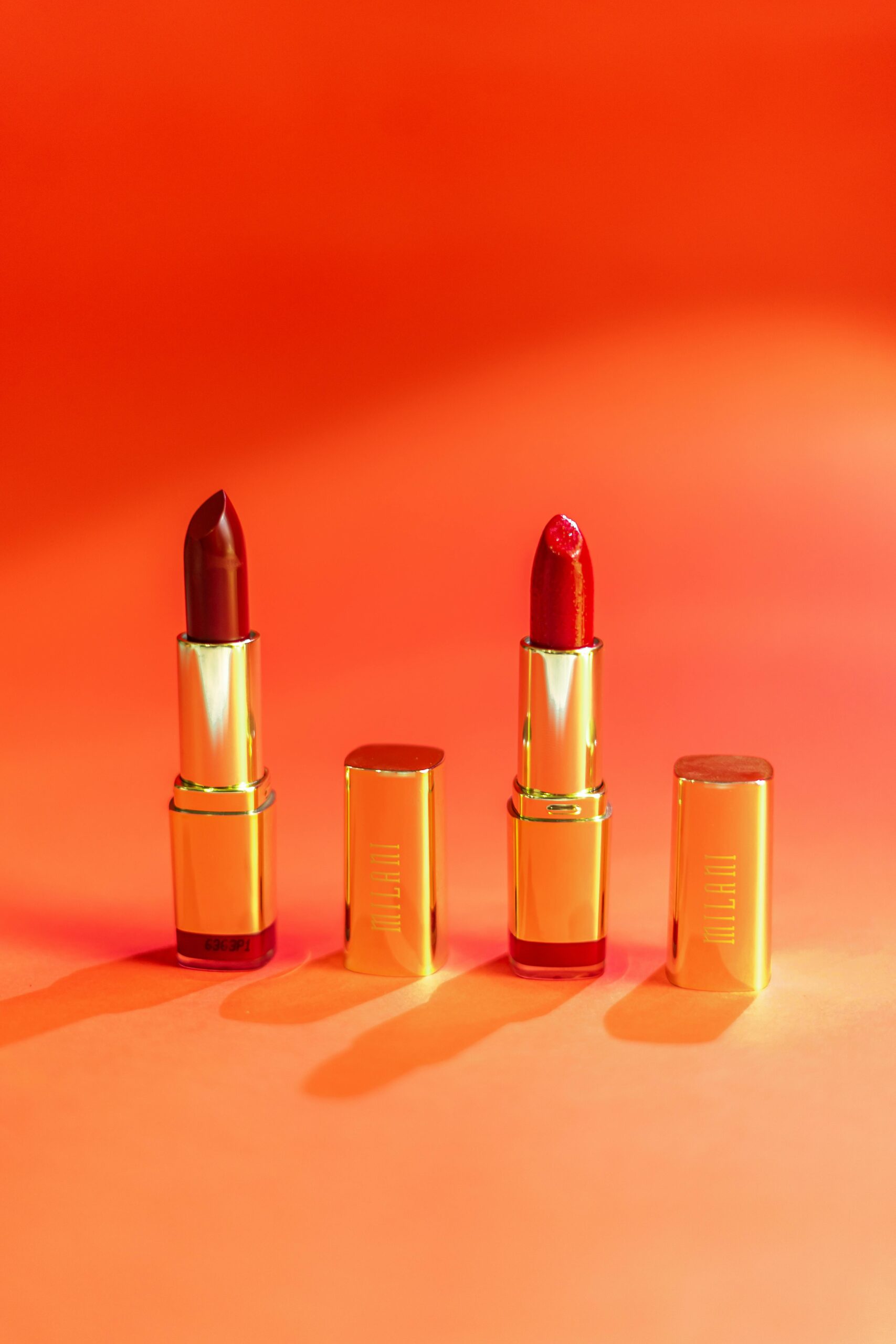 Striking image of red and burgundy lipsticks with gold packaging on a vibrant orange background.